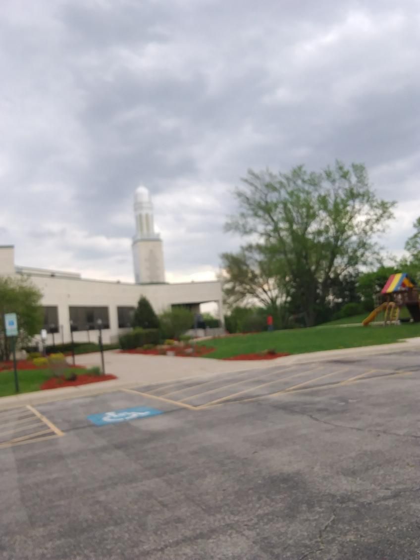 Empty parking lot with a building, tower, trees, and a playground under a cloudy sky