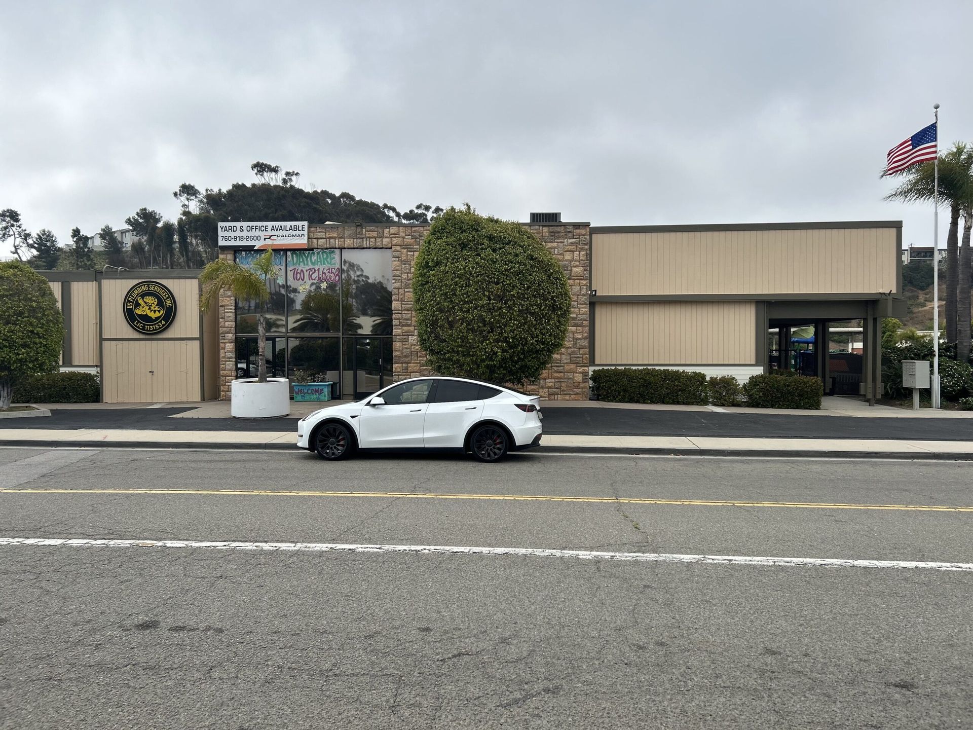 A white luxury SUV parked in front of a commercial building with stone accents and an American flag on a pole.
