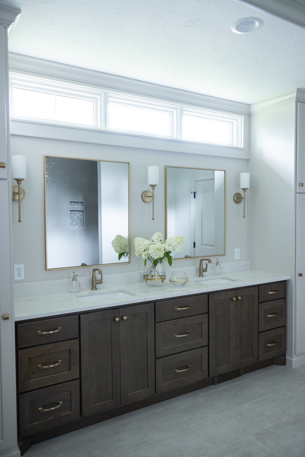 Double sink setup with two mirrors and flowers in a vase.