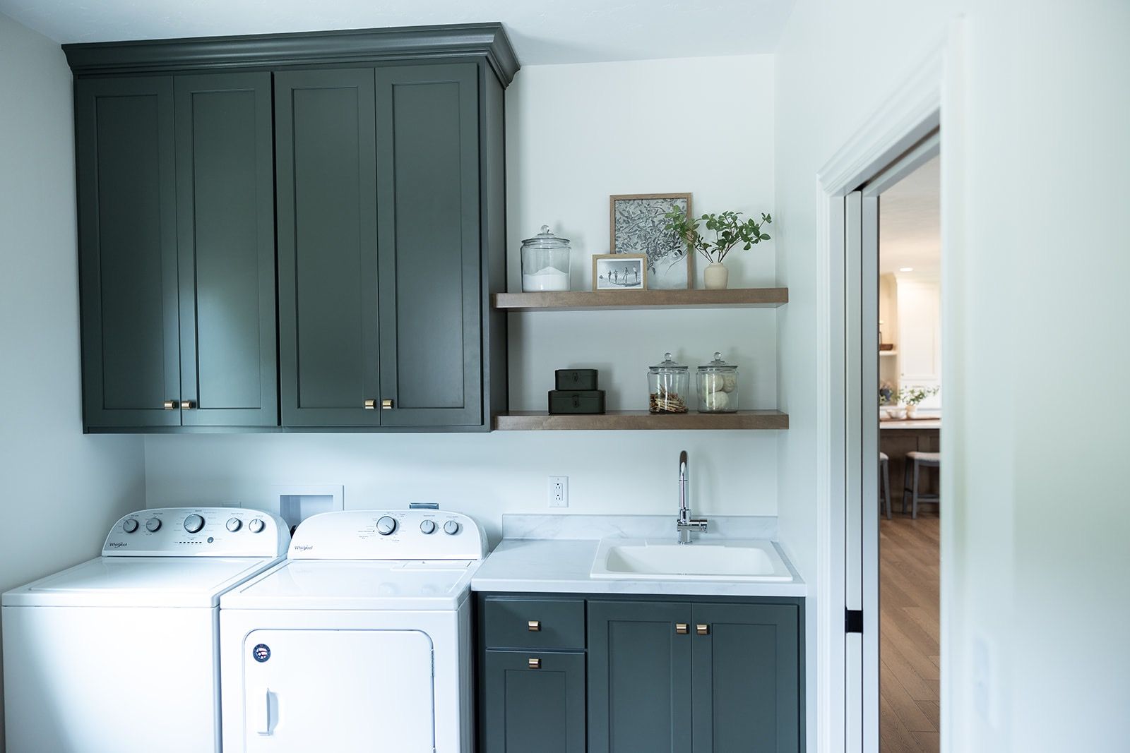 A blue laundry room with washer dryer combo and sink with decorations on the shelves above.