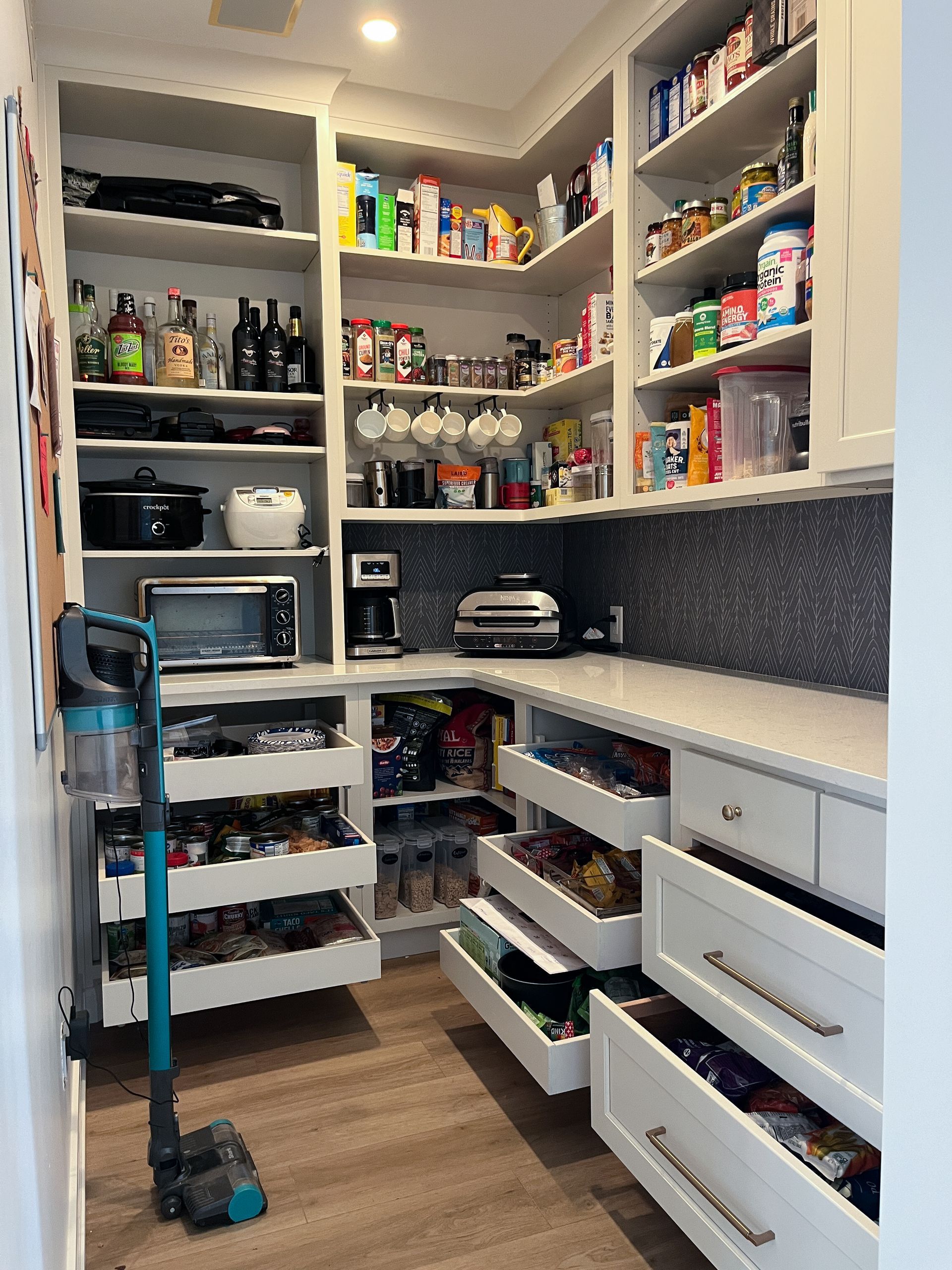 A full pantry with multiple shelves and drawers filled with food and ingredients with a microwave, toaster, and coffee machine.