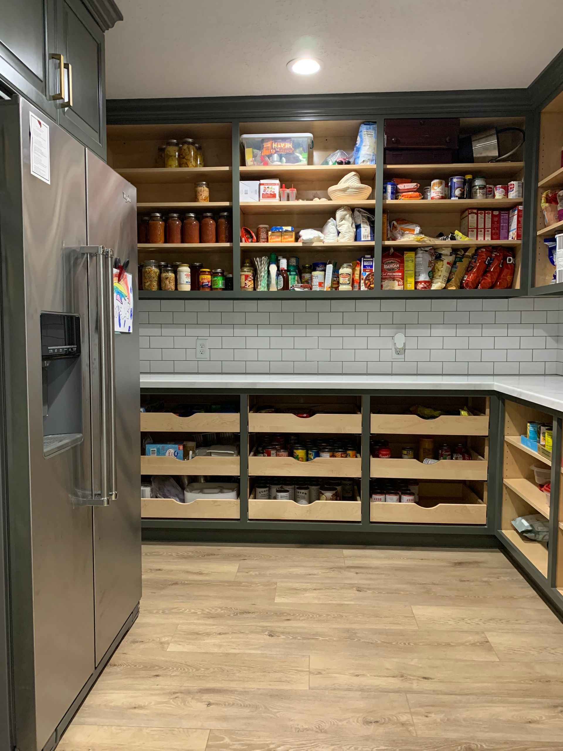 A full pantry with multiple shelves and drawers filled with food and ingredients next to a fridge 