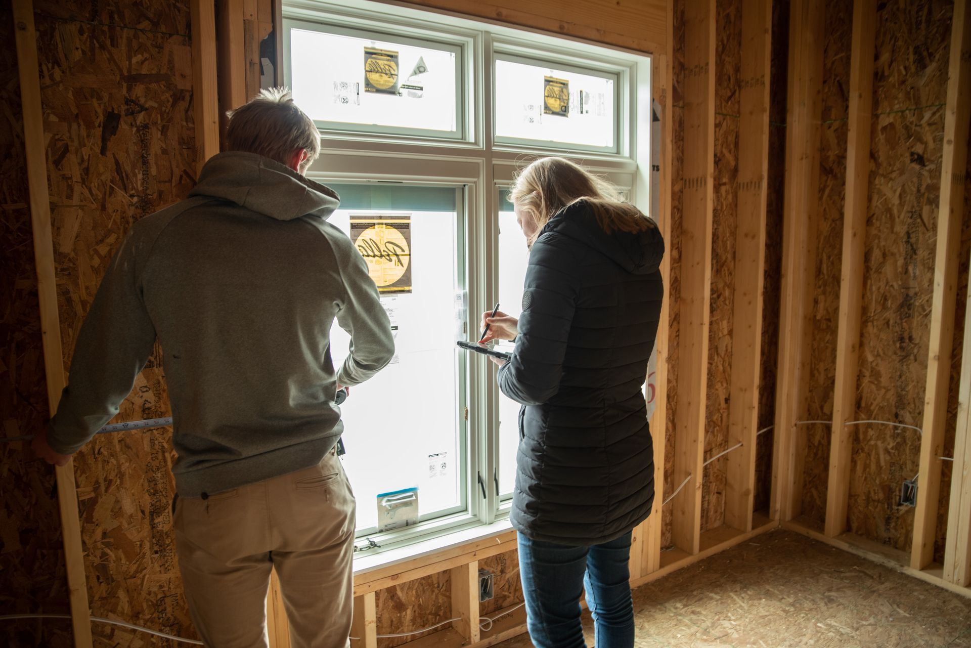 Two people checking windows they just installed into a room being built.