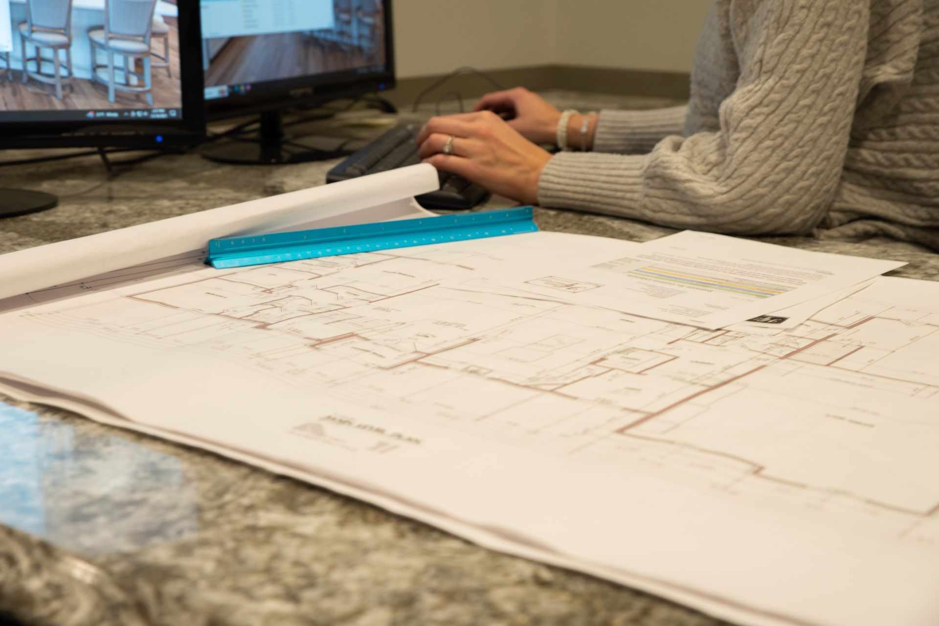 A blueprint for a house being referenced by a lady as she works on the computer.