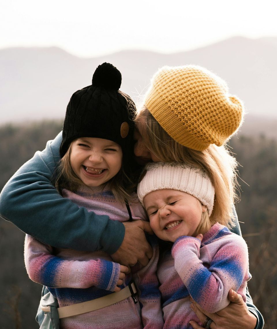 A woman is hugging two little girls wearing hats.