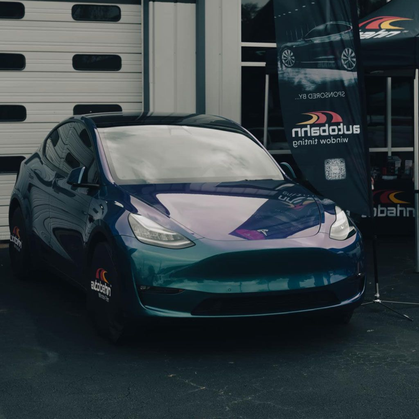 Dark blue Tesla in a garage, with a banner and garage door behind it