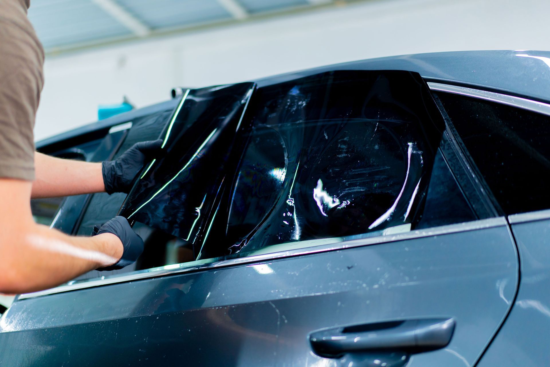 Person applying dark film to a car window with gloved hands