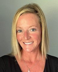 Smiling blonde woman in a black top against a light gray background.