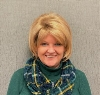 Woman smiling in a green plaid scarf against a beige wall