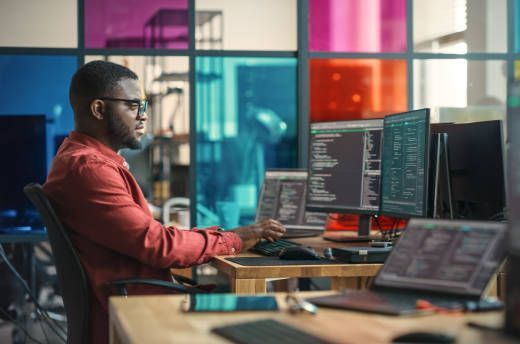 A man is sitting at a desk in front of three computer monitors.