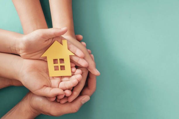 A person is holding a small white house in their hands.