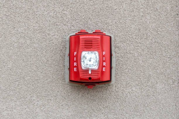 A red fire alarm is hanging from a pipe in a warehouse.