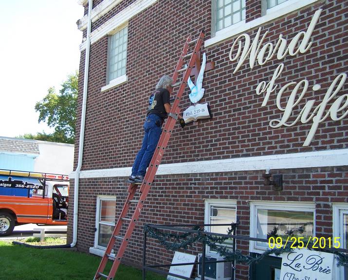 Man on ladder creating sign for church - custom wood, aluminum & lighted signs in Council Bluffs, IA