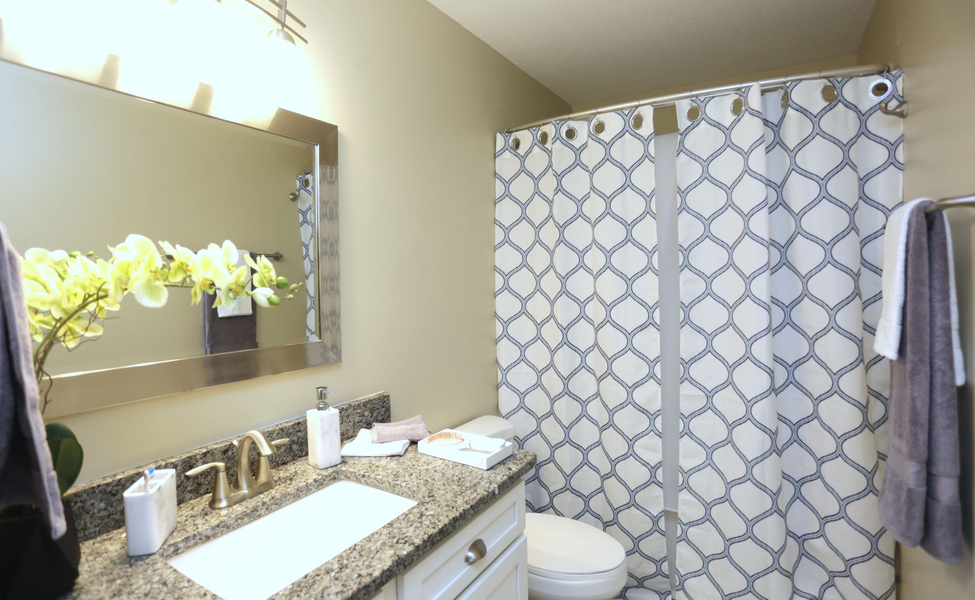 Bathroom with a white toilet, granite countertop, floral arrangement, and patterned shower curtain.
