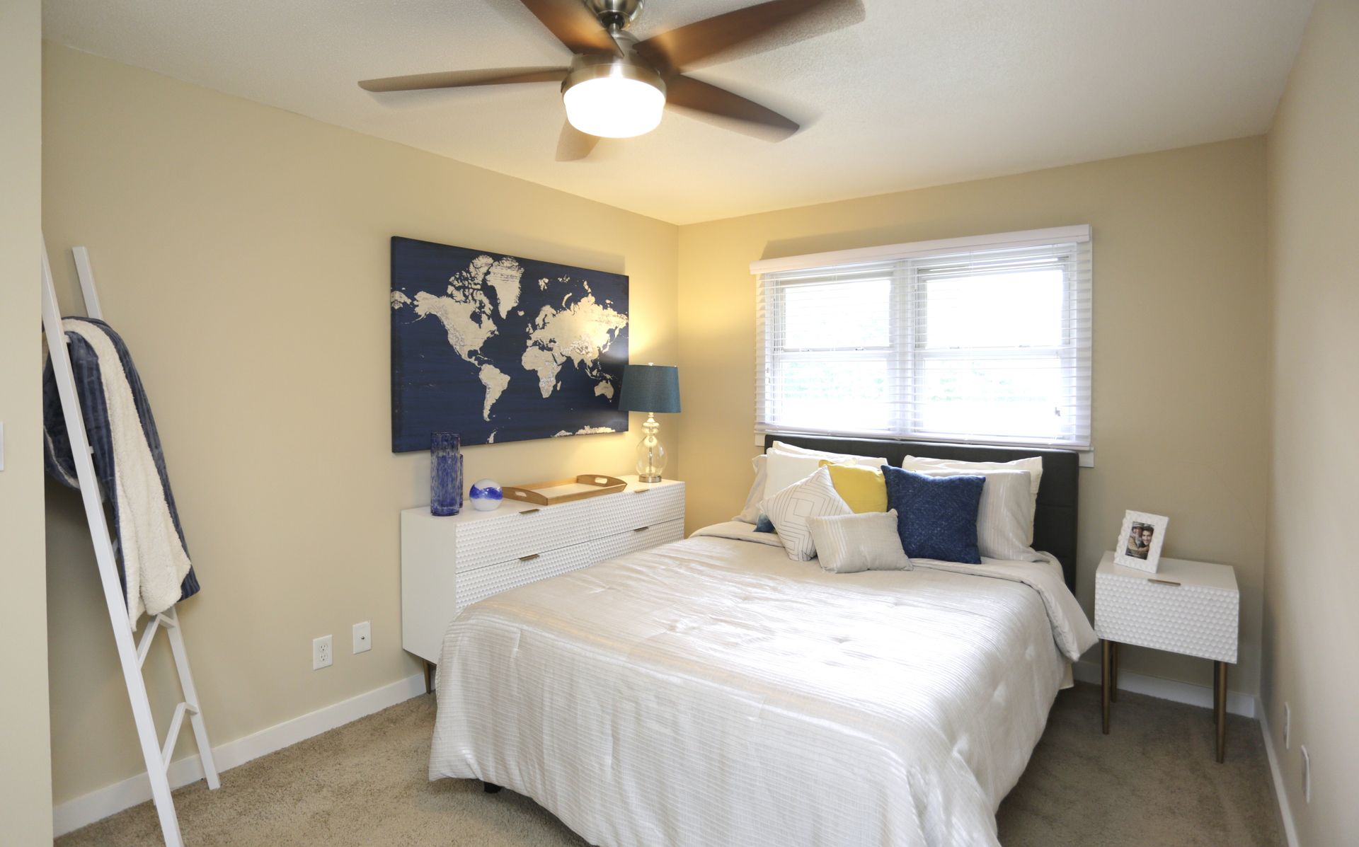 Bedroom with white bed, dresser, world map art, and a ladder-like coat rack.