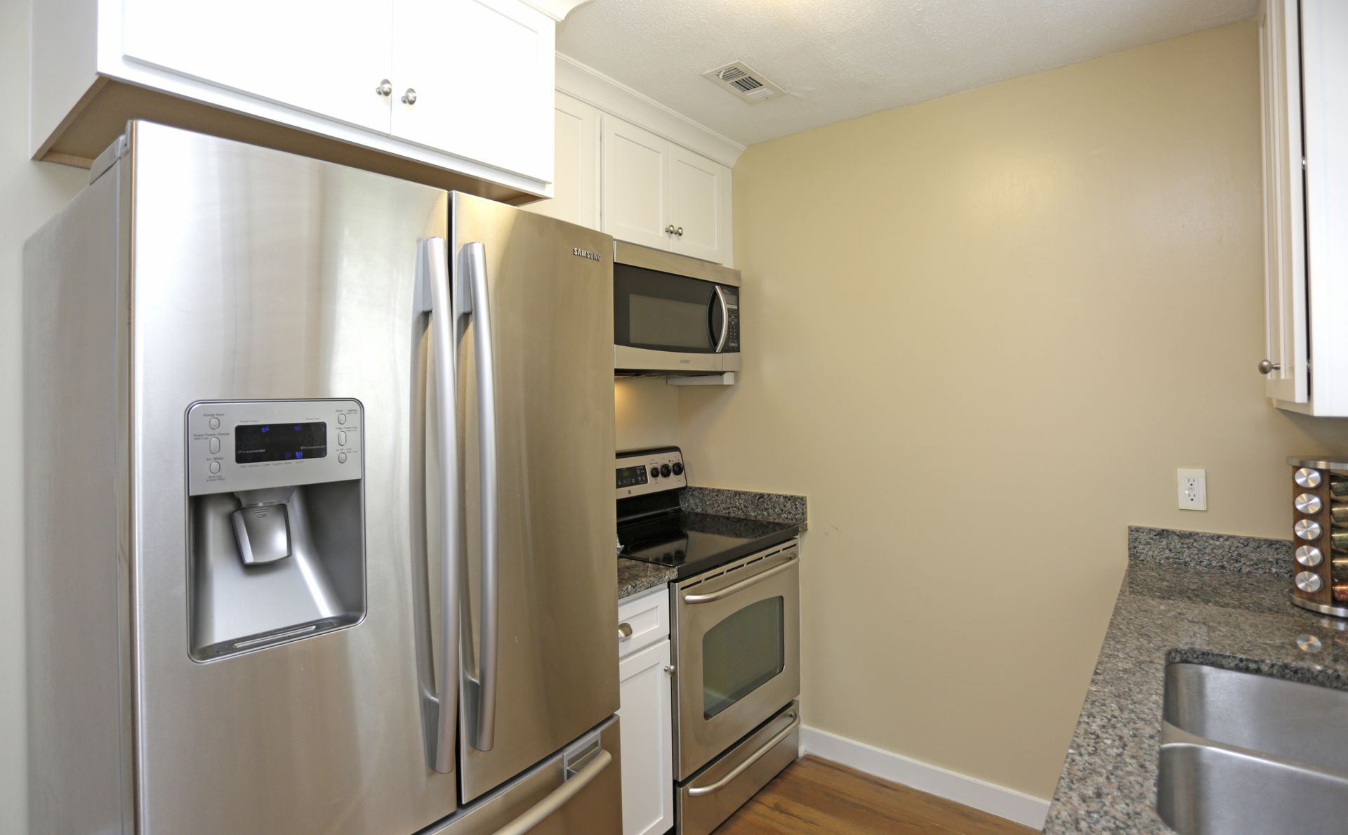 Stainless steel refrigerator and oven in a kitchen with white cabinets and a microwave.