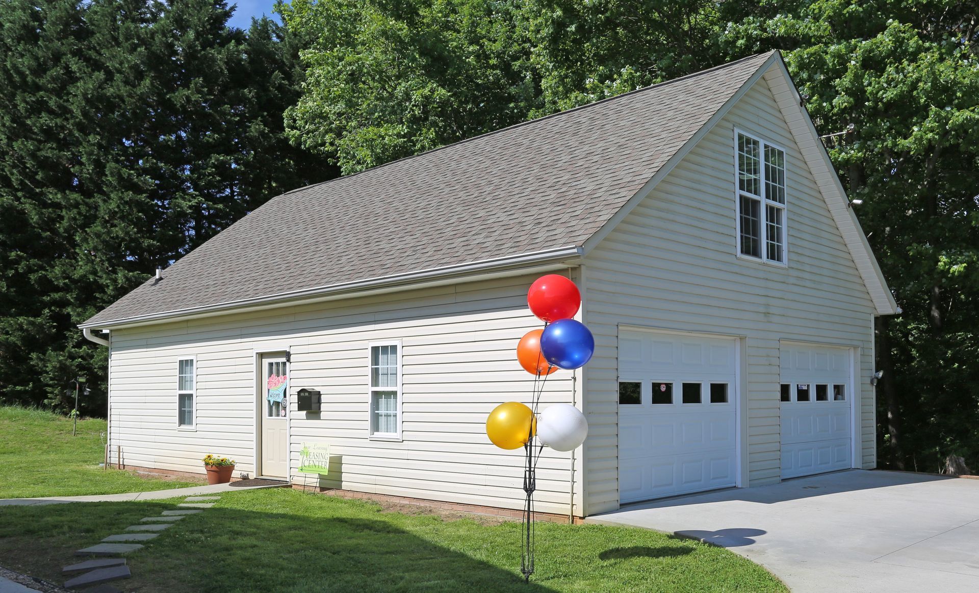 Two-story building with garage doors, siding, and a gabled roof. Balloons are tied to a pole on the lawn.