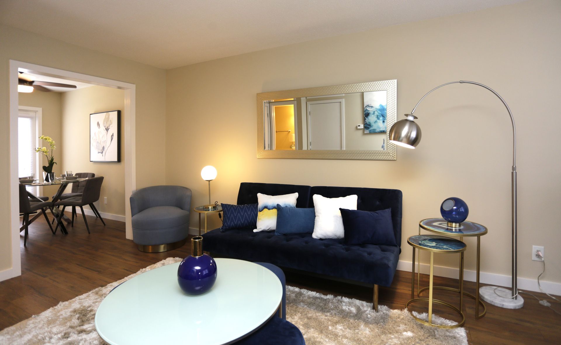 Living room with blue sofa, arched lamp, round coffee table, and open doorway to dining area.