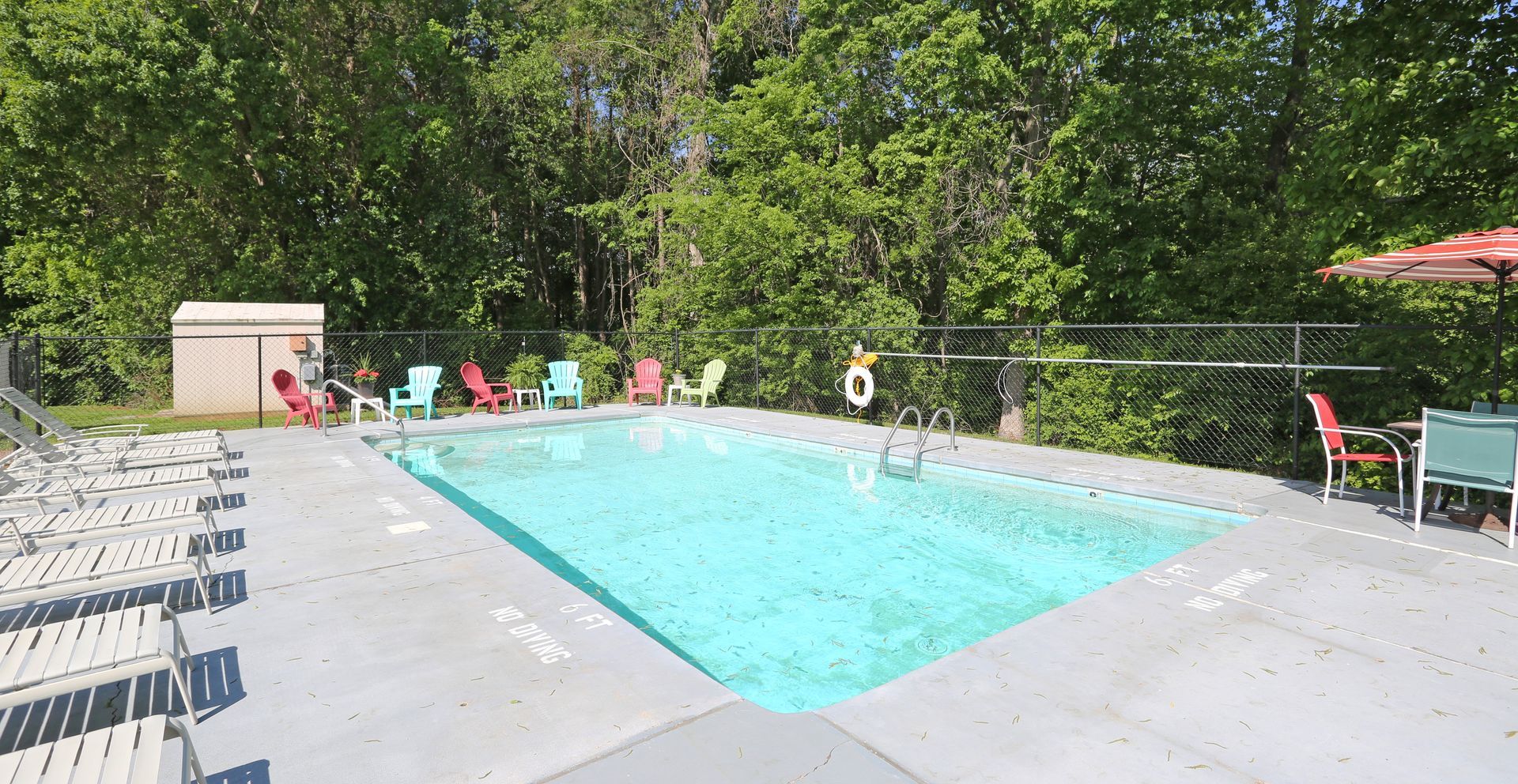 Swimming pool surrounded by chairs and trees, a life preserver hanging on the fence.