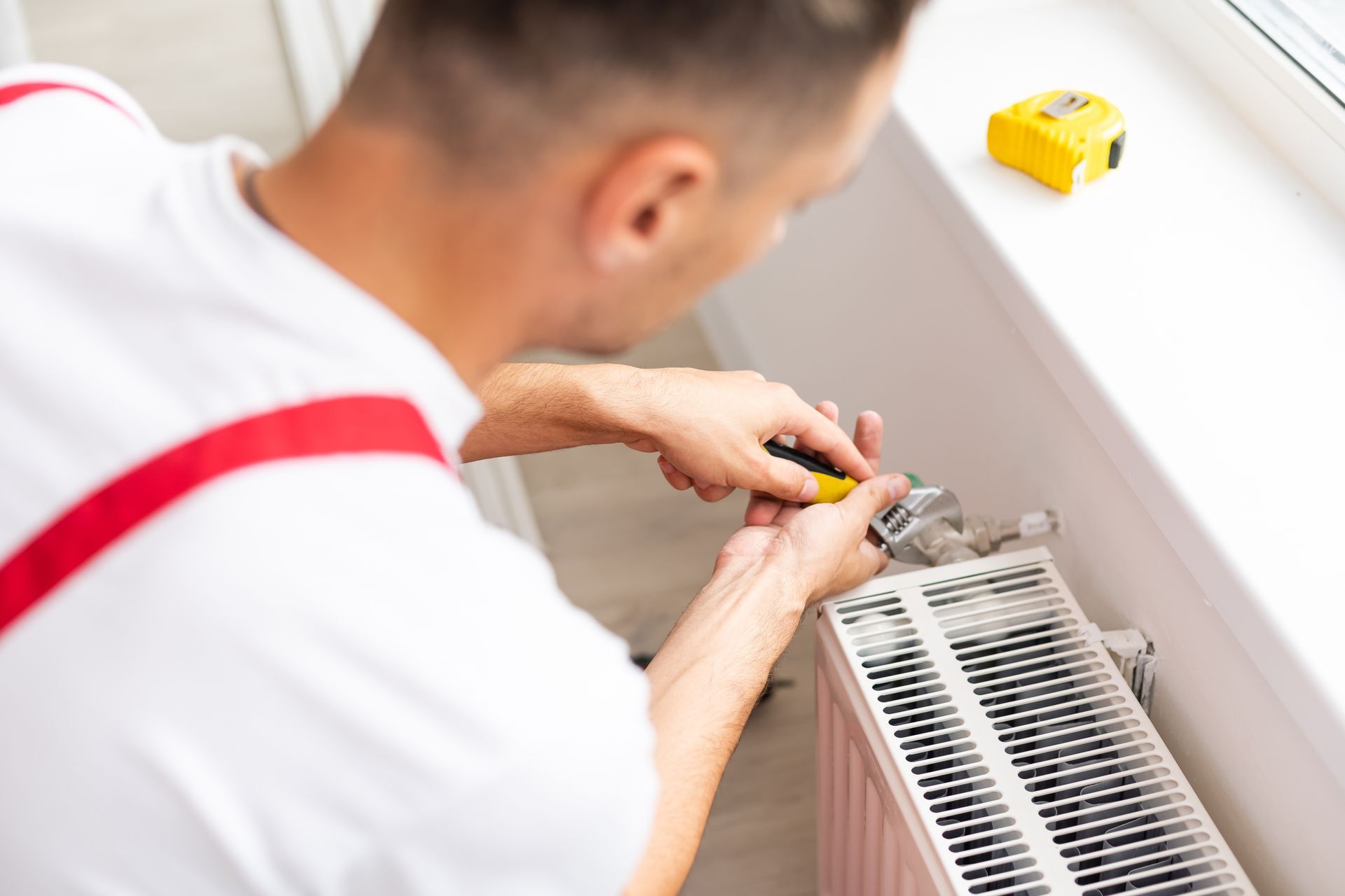 A man is fixing a radiator with a screwdriver.