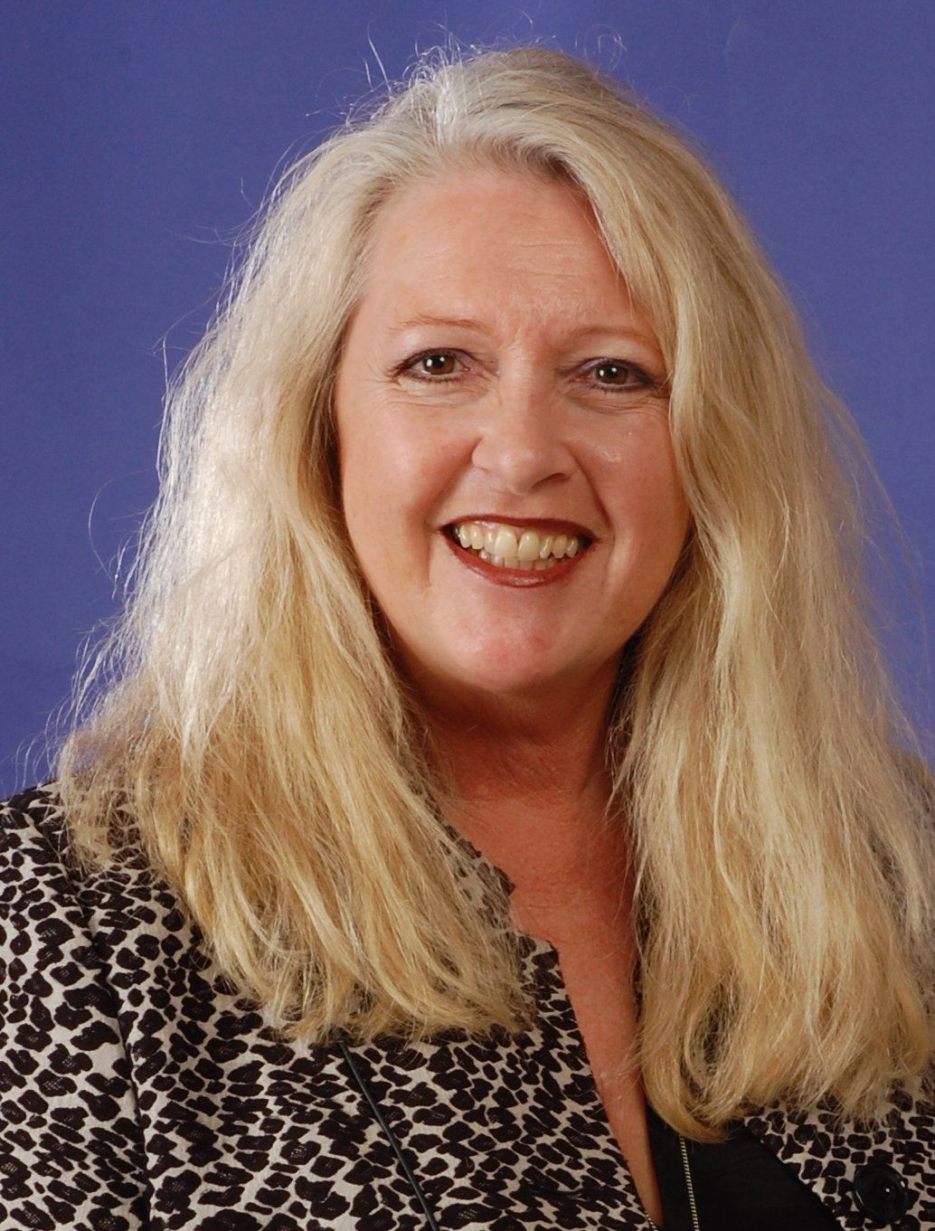 A woman with long blonde hair is smiling and wearing a leopard print jacket