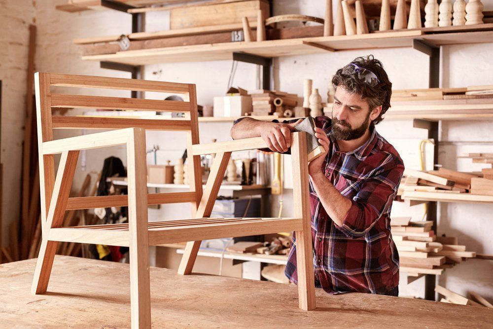 A man is working on a wooden chair in a workshop.