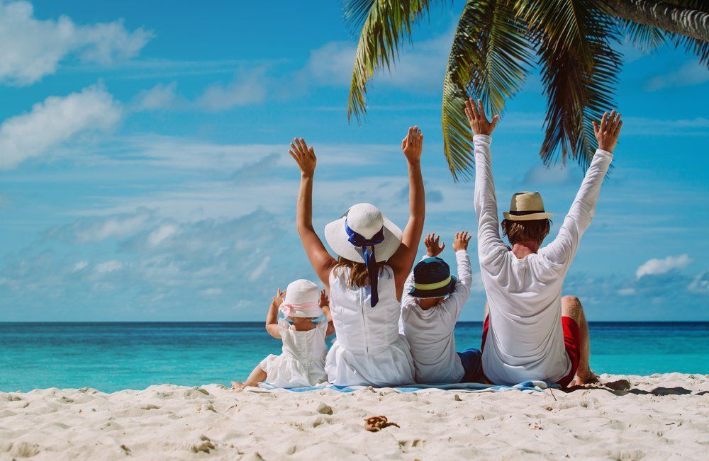 A family is sitting on the beach with their arms in the air.
