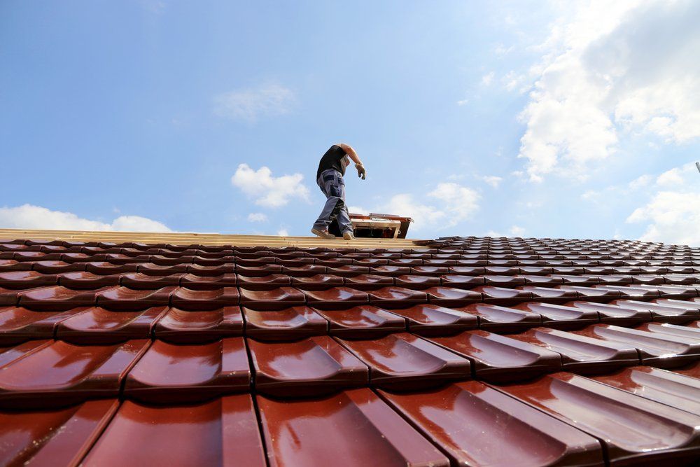 A man is standing on top of a roof with red tiles.