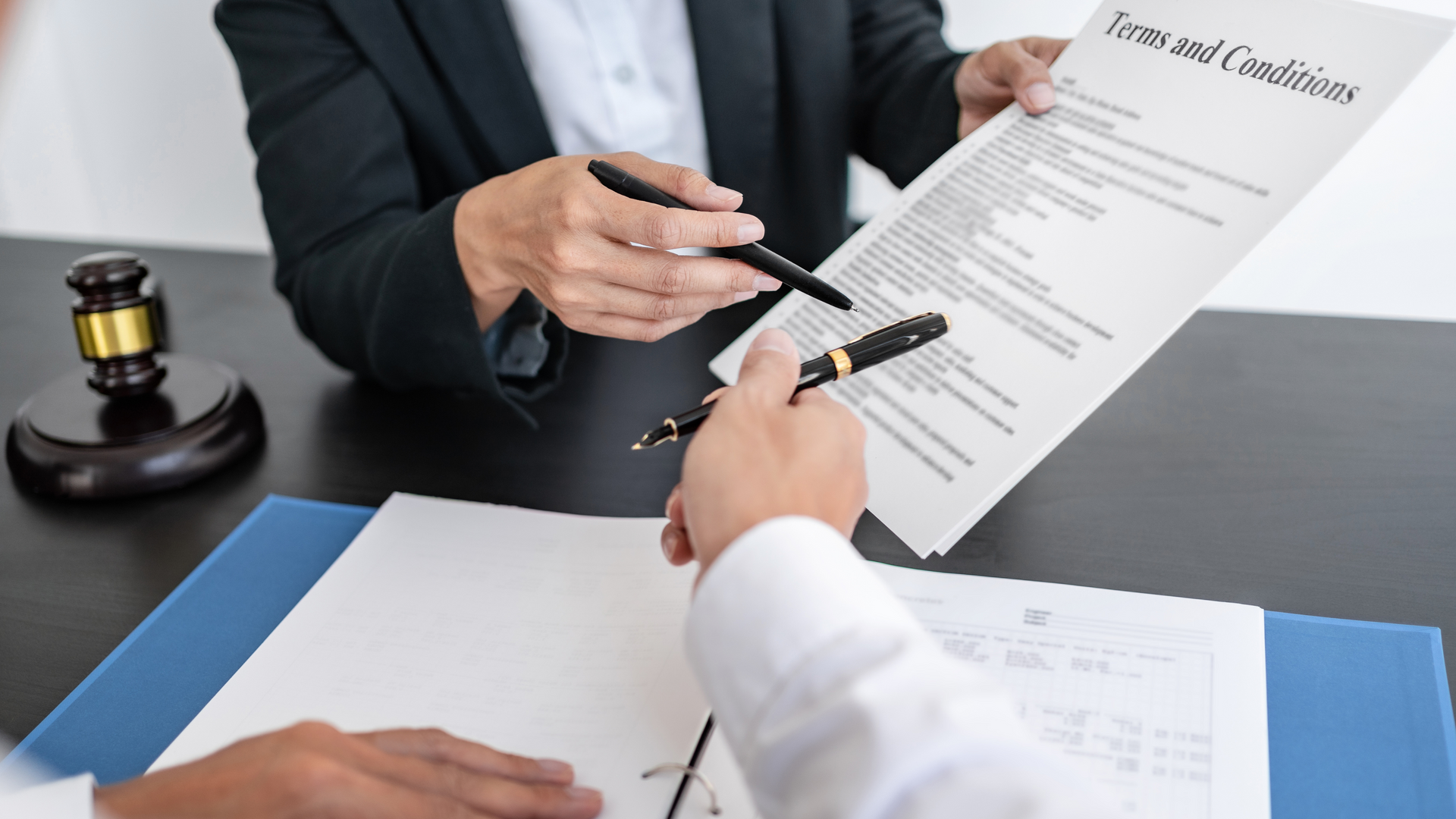 Lawyers reviewing a contract document across a desk, with a gavel nearby