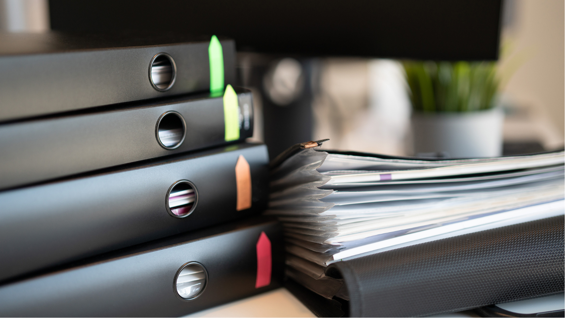 Stacked black binders beside a pile of papers in an office setting