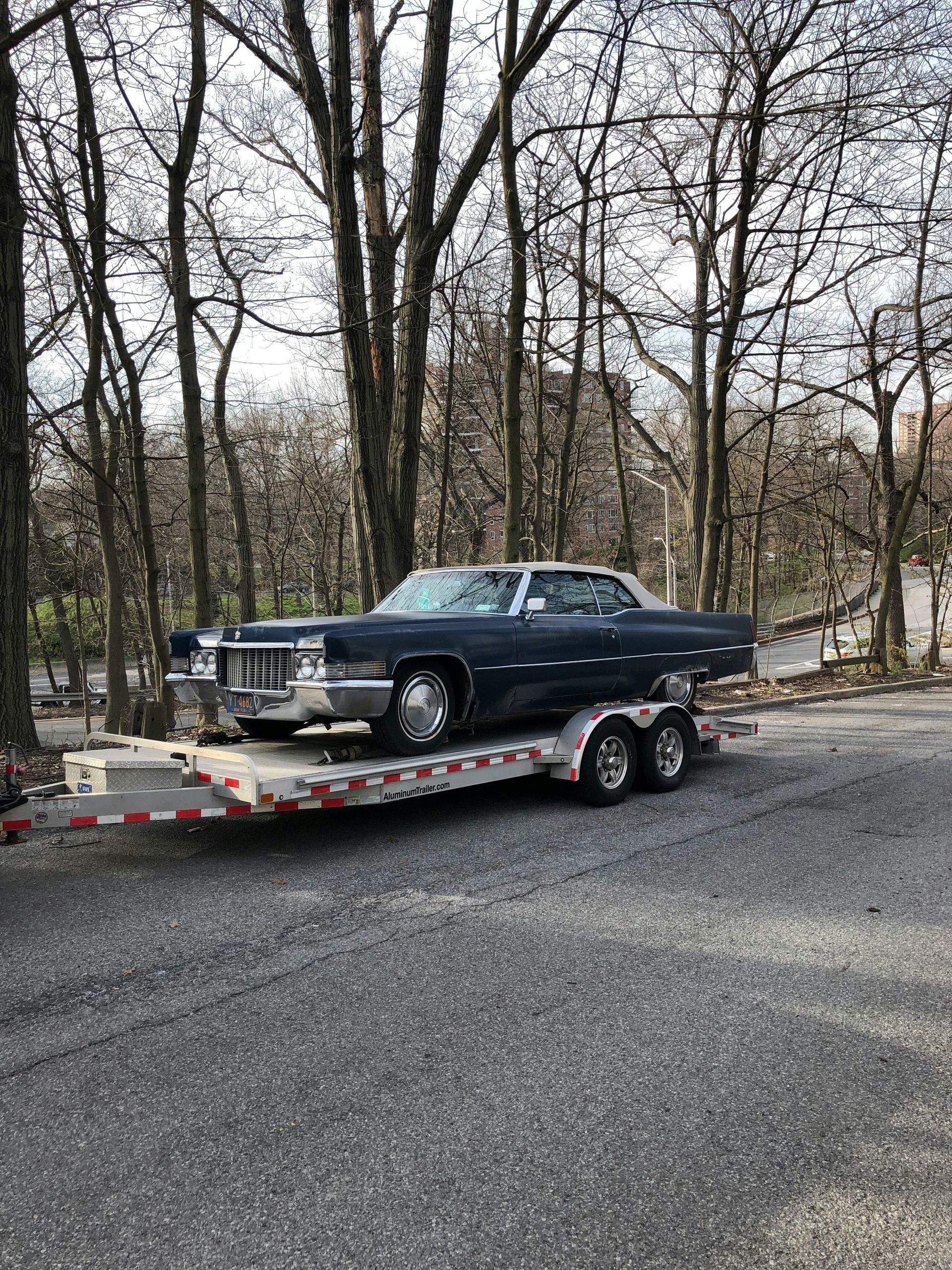 Blue vintage car on a trailer in a tree-lined area.