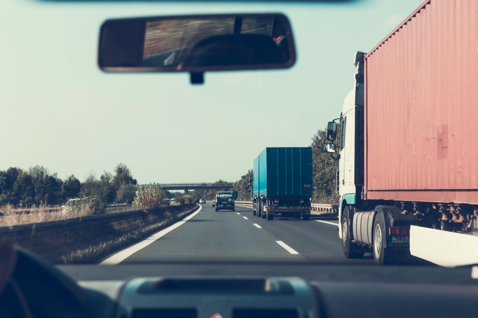View from inside a car on a highway, following semi-trucks under a bright sky.