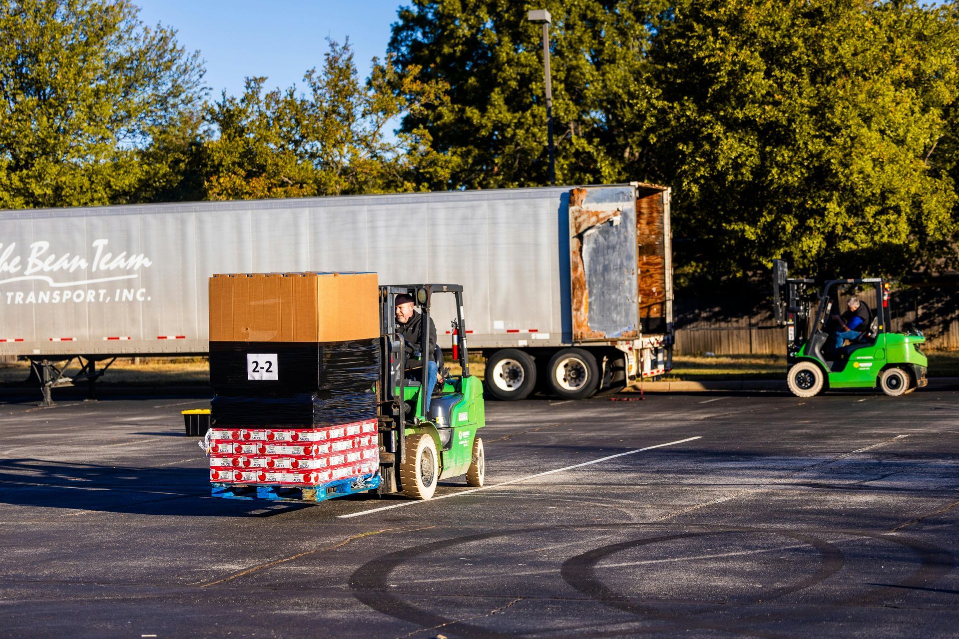 Two forklifts loading boxes onto a truck trailer in an outdoor parking lot.