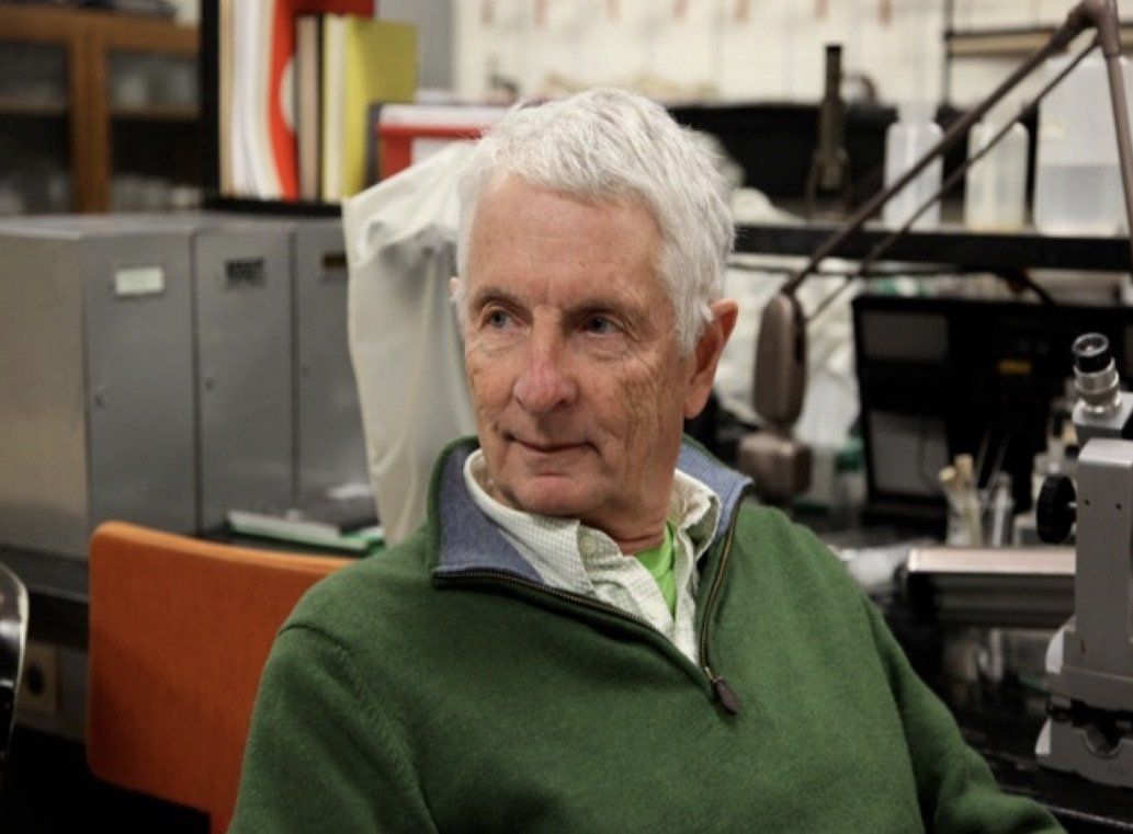 A man in a green sweater is sitting in a lab