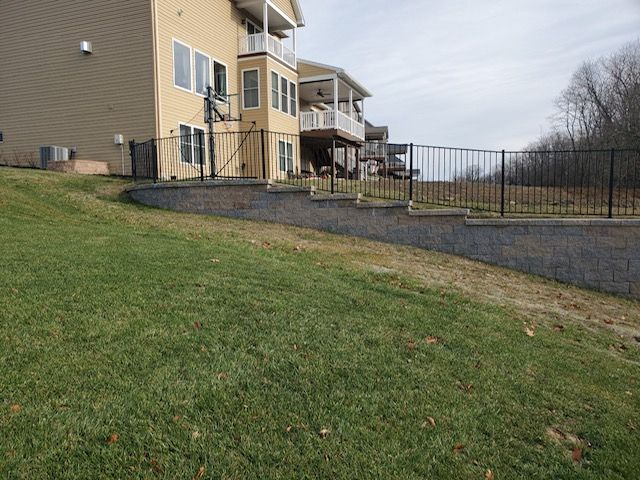 A large house is sitting on top of a grassy hill next to a fence.