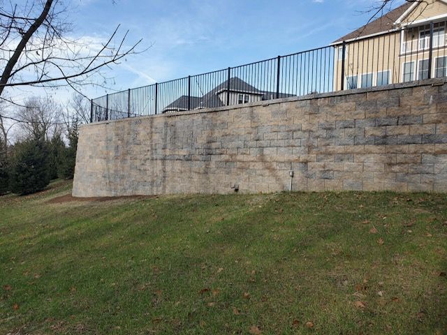 A large stone wall with a metal fence surrounding it in front of a house.