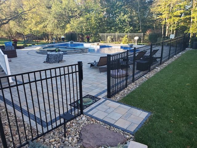 A black fence surrounds a patio with a pool in the background.