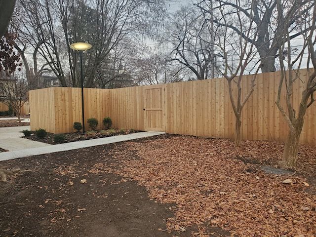 A wooden fence is surrounded by trees and leaves in a park.