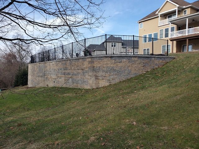 A large house with a fence around it is sitting on top of a grassy hill.