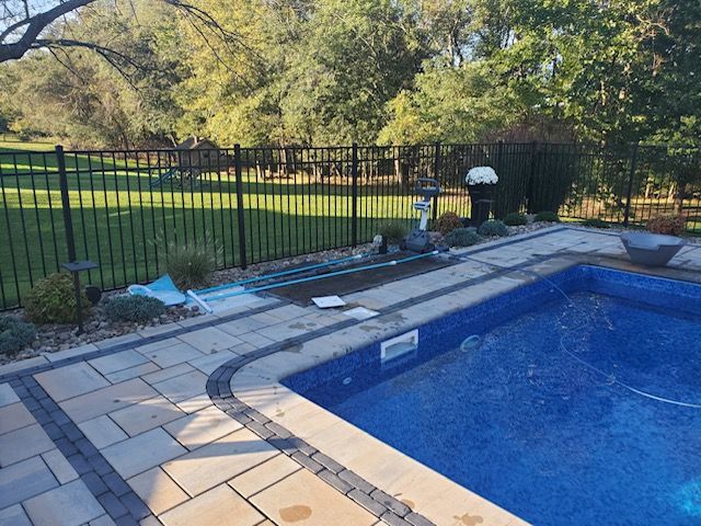 A large swimming pool is surrounded by a fence and a patio.