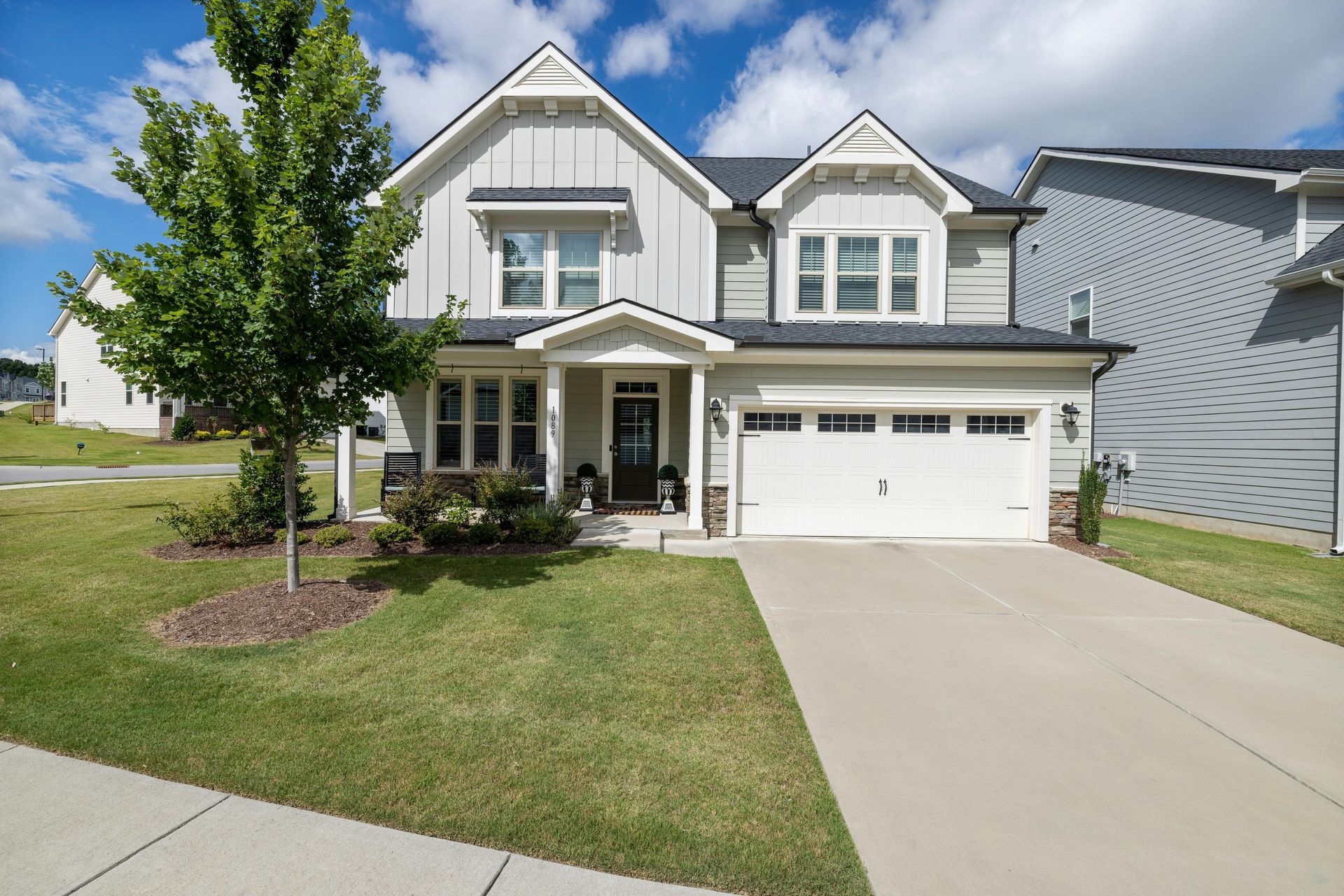 A large white house with a garage and a tree in front of it.