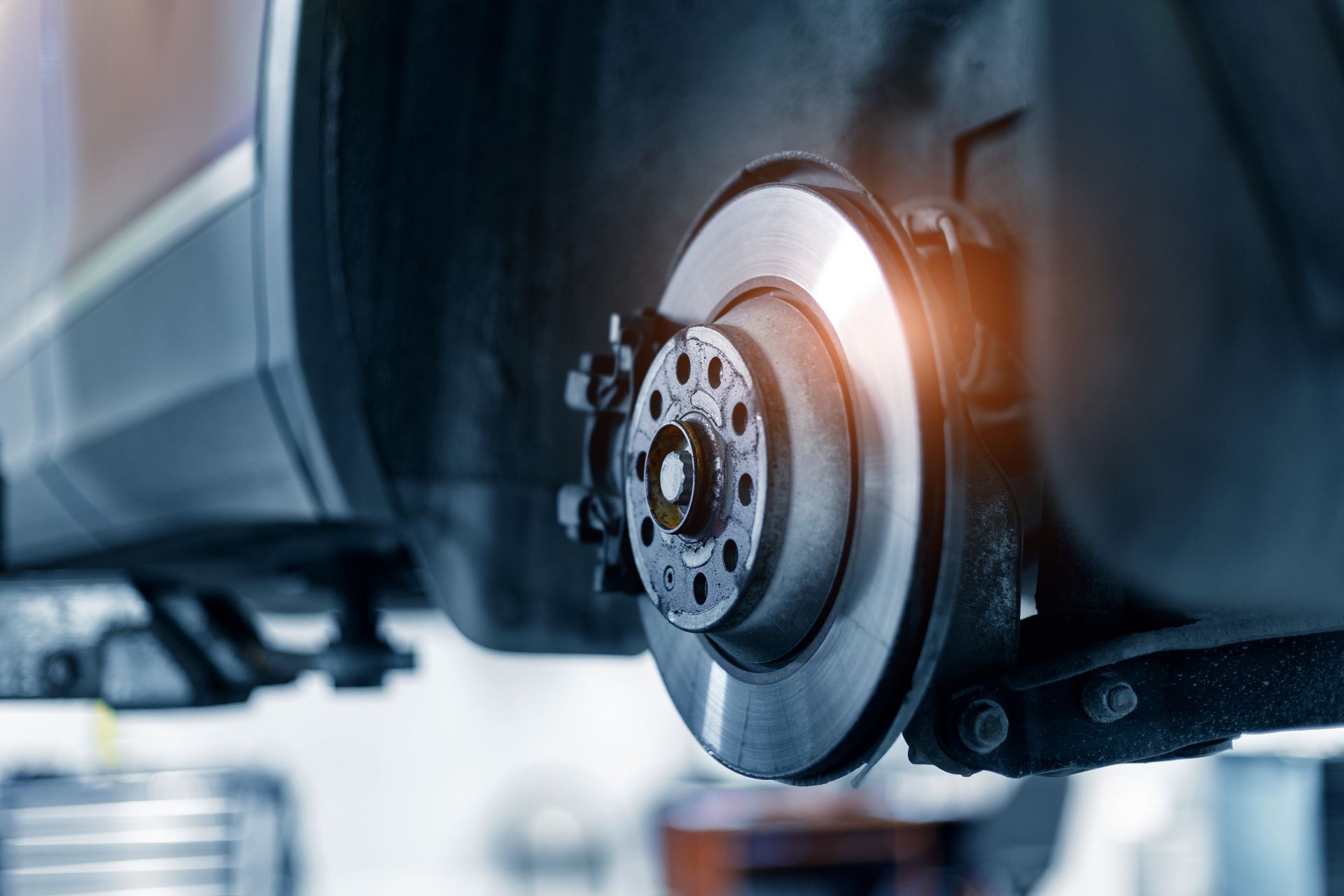 Close-up of a car brake disc and caliper with a glowing orange reflection in a garage.