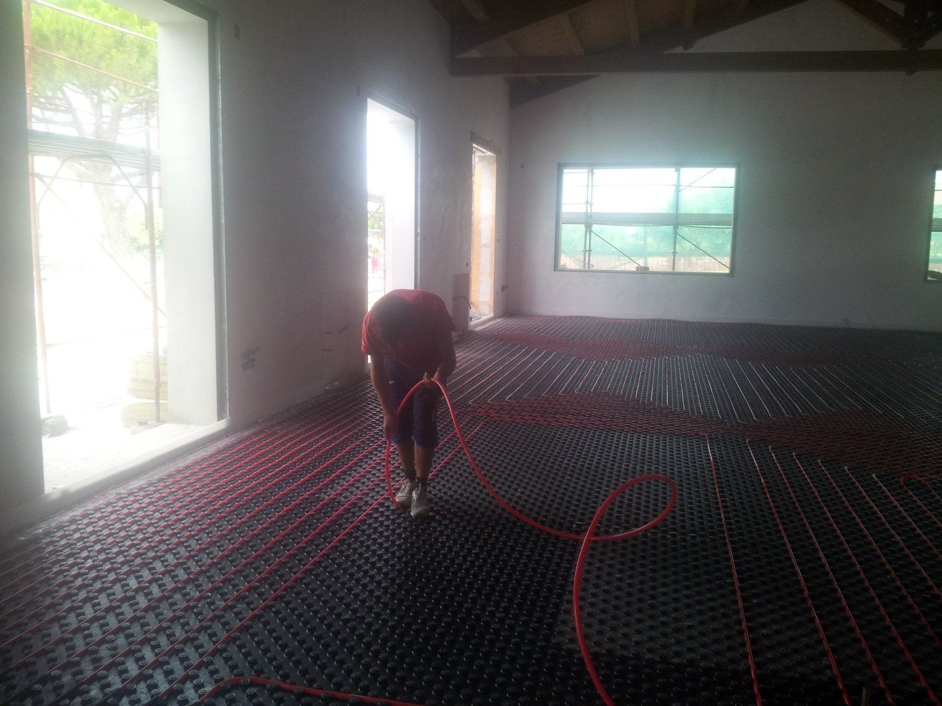 Una persona installa i tubi del riscaldamento a pavimento radiante all'interno di un pannello isolante a griglia in un edificio non ancora ultimato.