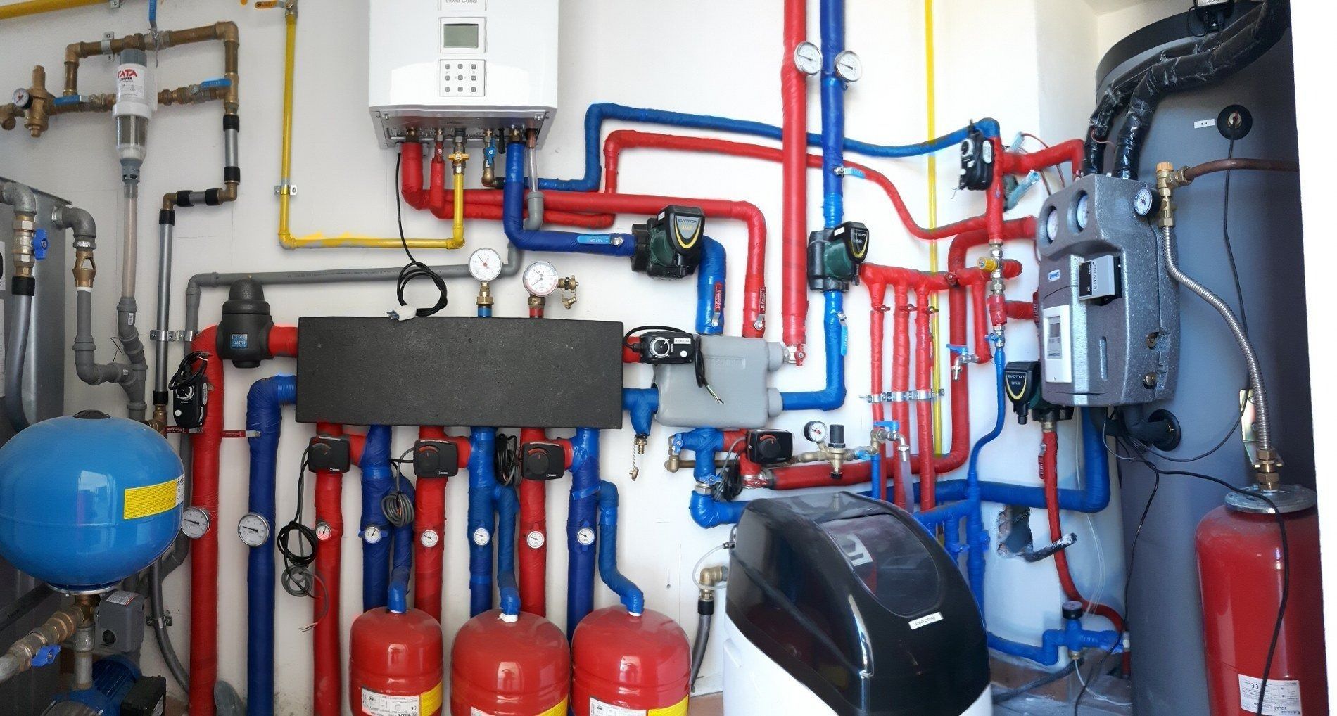 Una complessa parete di servizio per la sala caldaie, con tubature multicolori, serbatoi d'acqua e comandi per l'impianto di riscaldamento industriale.
