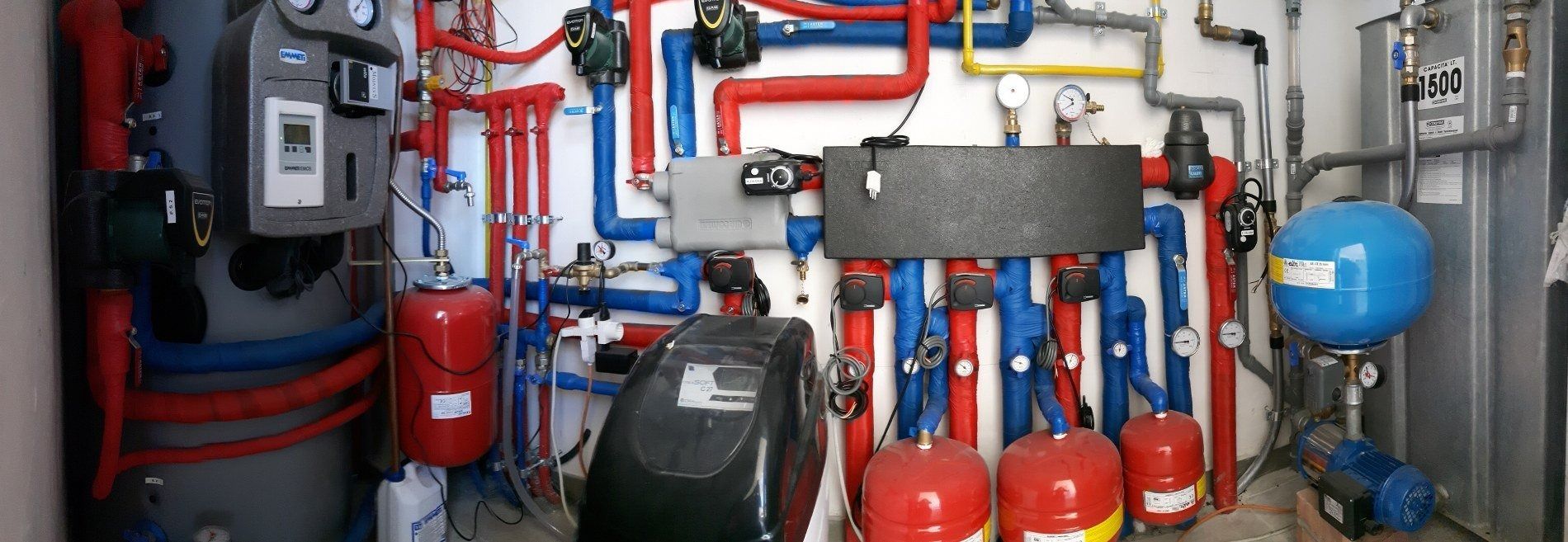 Una complessa sala macchine con numerose tubature isolate di colore rosso e blu, caldaie e serbatoi a pressione blu.
