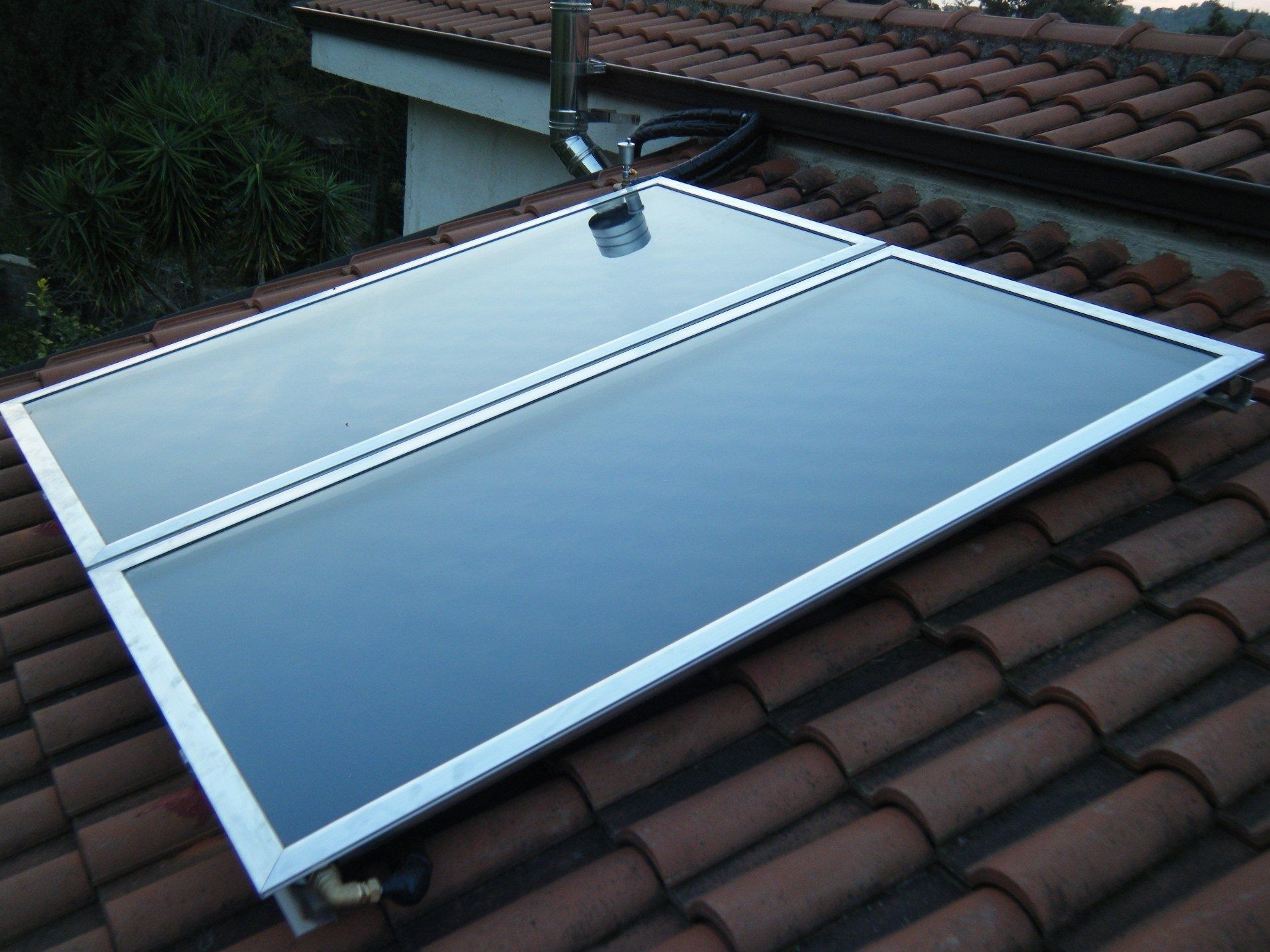 Due pannelli solari termici montati su un tetto di tegole marroni.