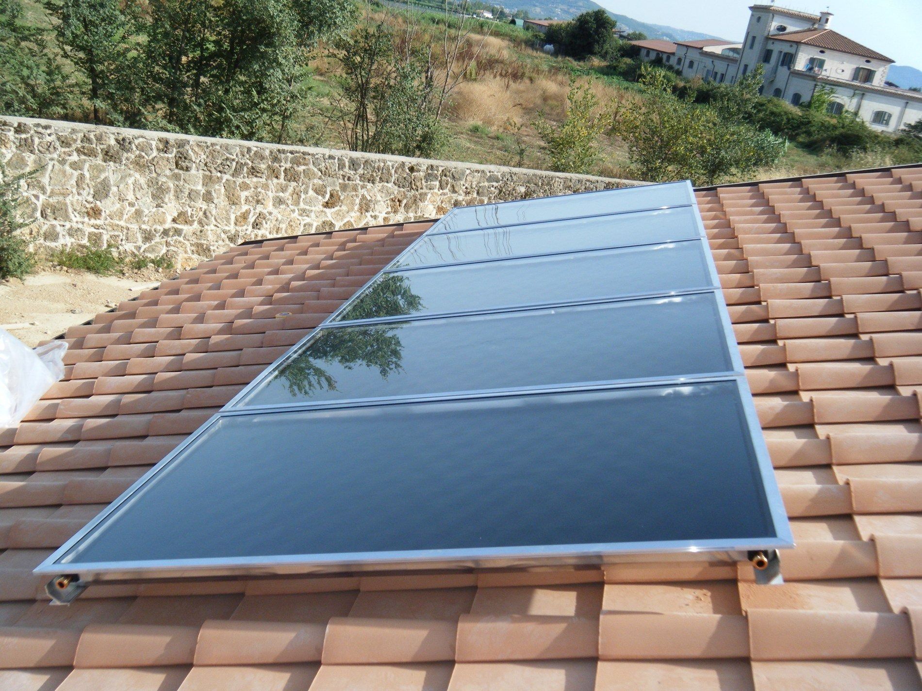 Pannello solare termico installato su un tetto di tegole in terracotta in un ambiente esterno soleggiato.