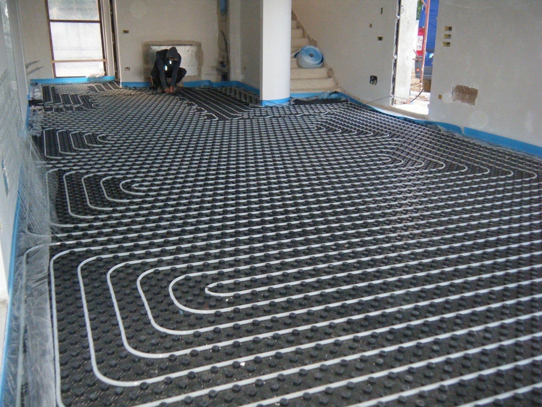 Tubi per il riscaldamento a pavimento installati su un tappetino isolante scuro e irregolare in una stanza in fase di ristrutturazione.