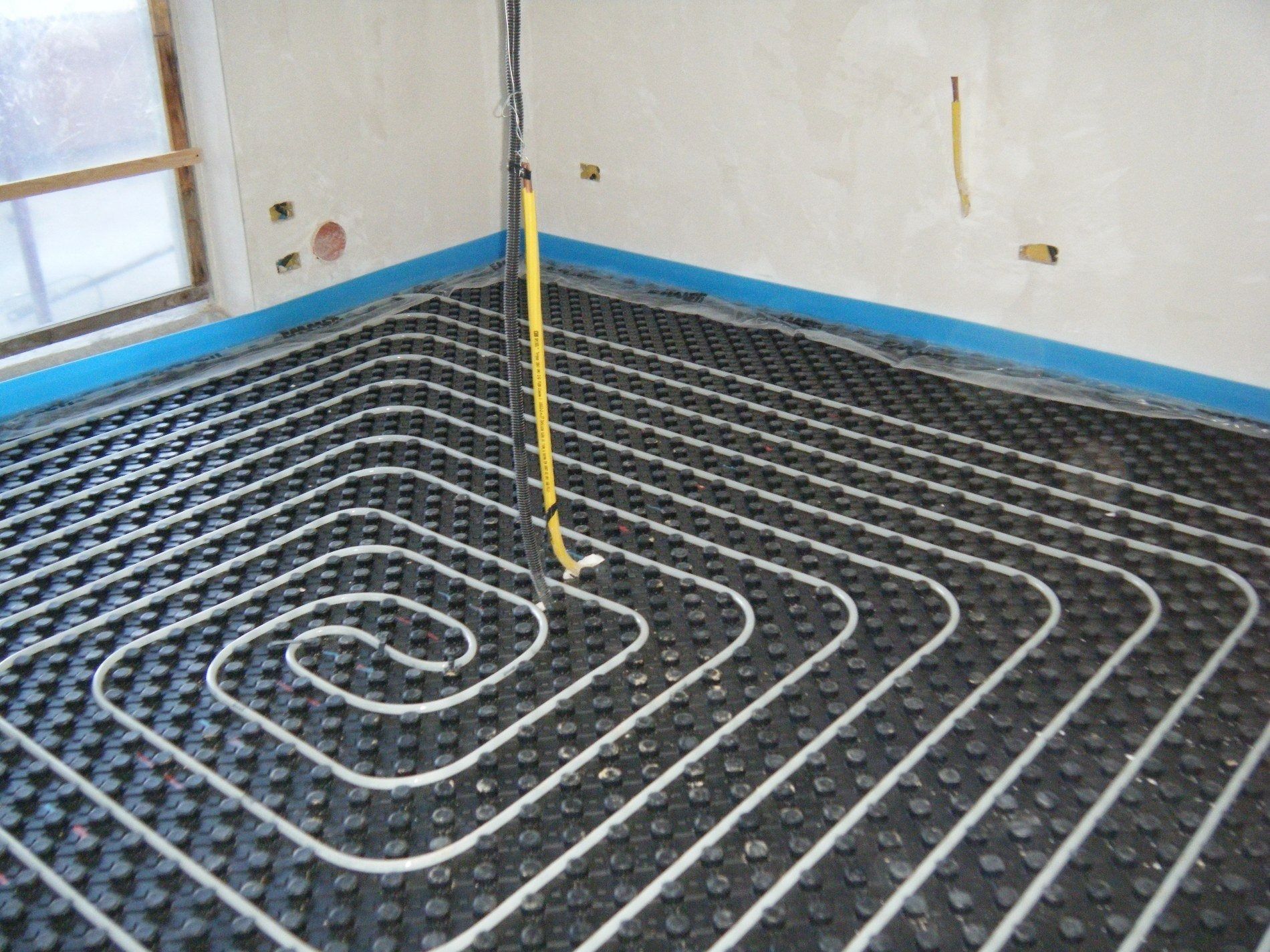 Tubi per riscaldamento a pavimento radiante installati a spirale su un battiscopa nero con borchie in una stanza non rifinita.