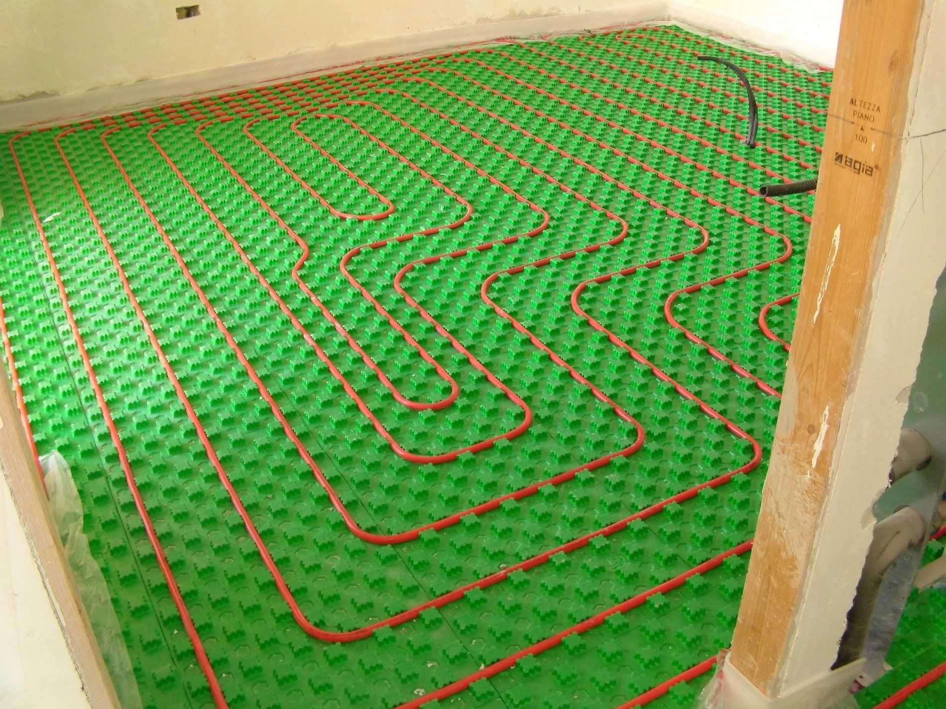 In una stanza, i tubi del riscaldamento a pavimento radiante sono installati con un motivo a serpentina sopra pannelli isolanti modulari verdi.